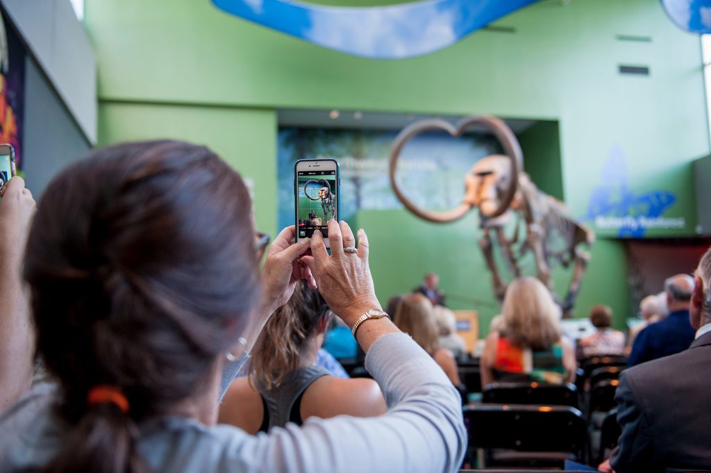 woman takes a cellphone photo of Florida museum mammoth and an event speaker