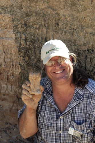 man at fossil dig holding up large square fossil bone