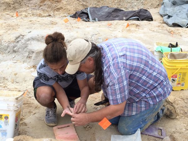 researcher and student looking closely at a fossil at a dig site
