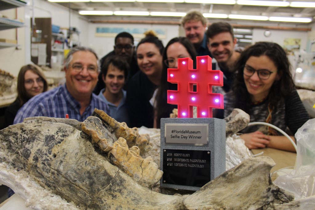 hashtag trophy sitting on a fossil surrounded by researchers and students