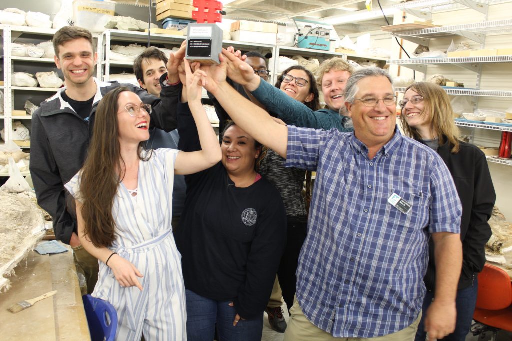 paleontology students reaching up to tough a trophy