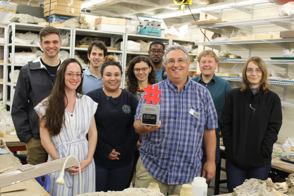 researchers with a trophy surrounded by fossils in a lab