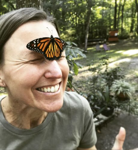 A woman has a monarch butterfly on her face.