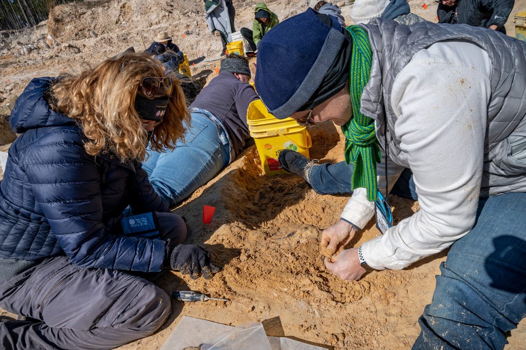 Participants sit on the ground digging in the red clay with their hands
