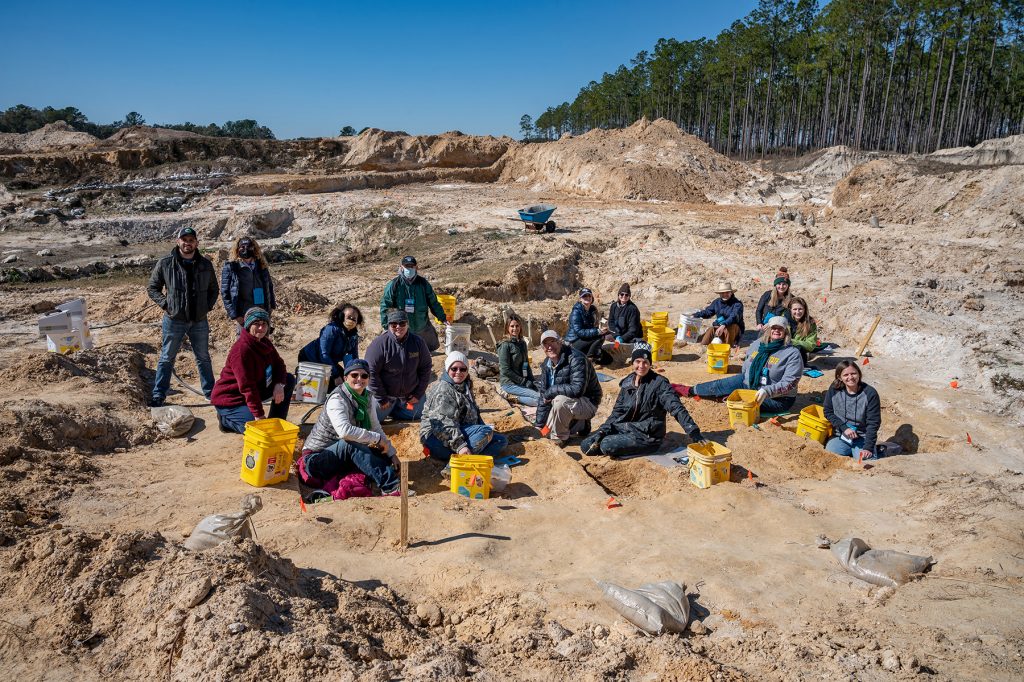 group photo with everyone sitting in the excavation site at the Montbrook fossil dig