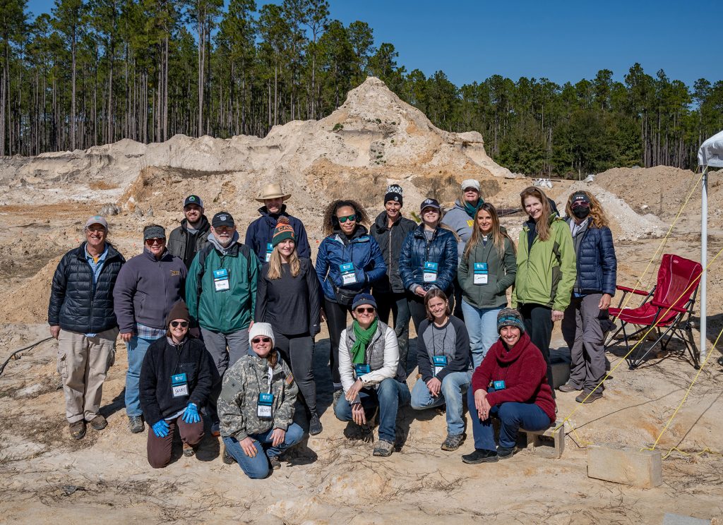 Group photo in front of the large dirt mounds at the Montbrook fossil dig.