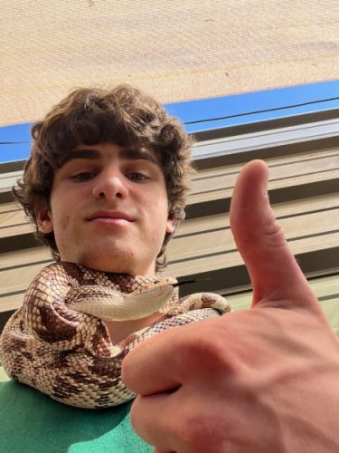 portrait of intern Wes Melkin with a snake around his neck and giving a thumbs up 