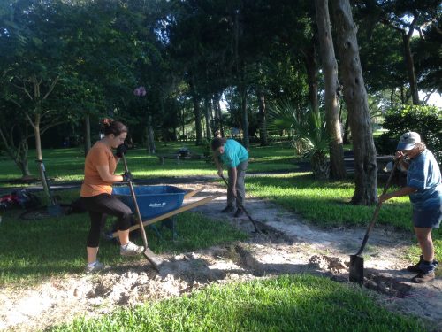 people shoveling dirt into wheelbarrow