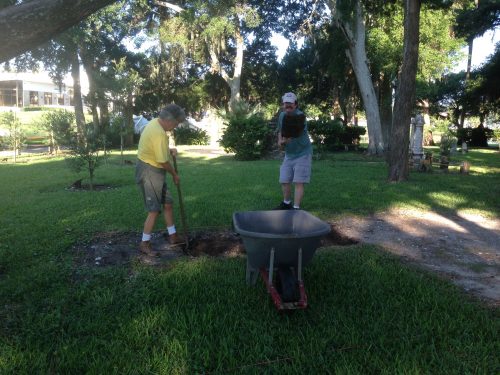 people shoveling dirt into wheelbarrow