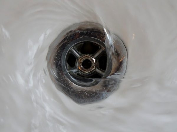 close up of water going down a metal drain in a white ceramic sink