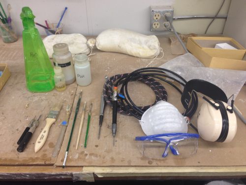 Top left to bottom right: spray water bottle, lubricating oil for airscribes, acetone, PVA, carbide picks, brushes, a PaleoAro and a microjack (airscribes of different sizes and strengths), dust mask, goggles, and ear muffs for noise protection.