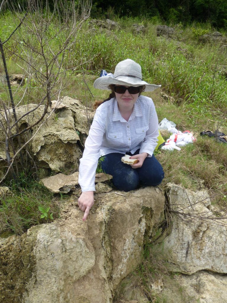 Carolyn Thornton sitting on the ancient algal deposit, pointing to a fossil leaf