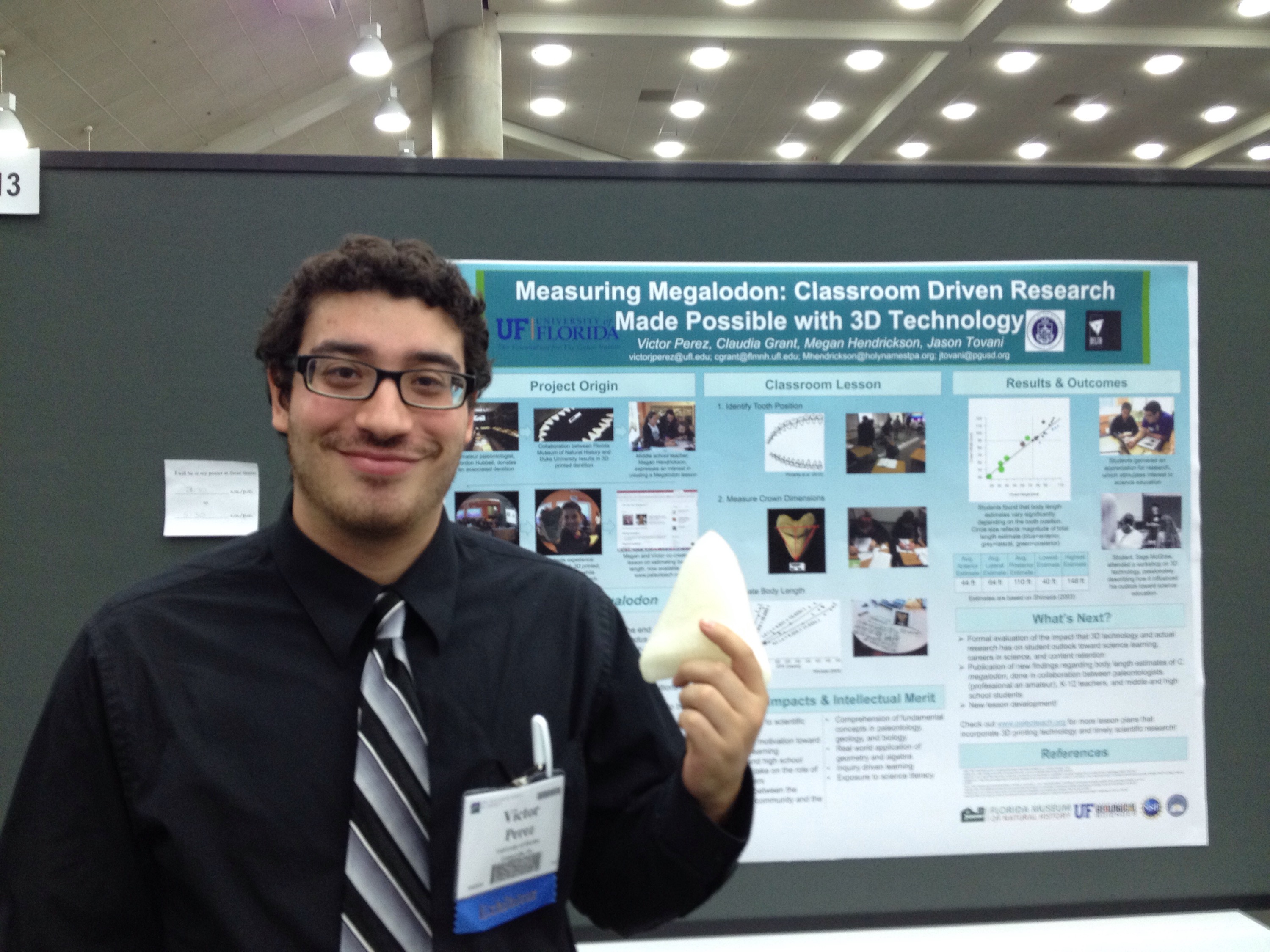 PhD student Victor Perez holds a 3D printed megalodon tooth in front of his research poster.