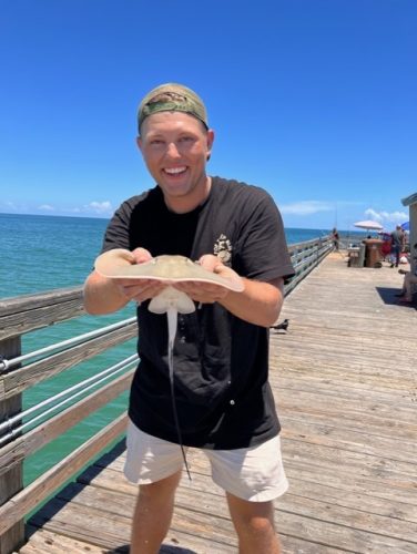 Man smiling and holding stingray on peir