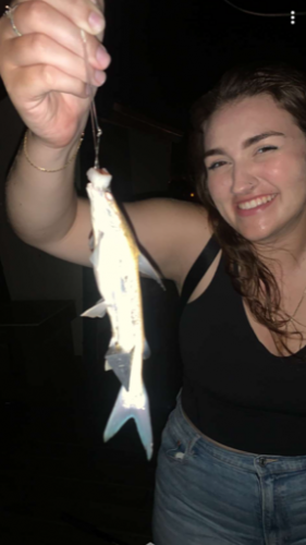 Smiling woman holding a small fish at night