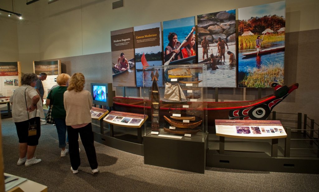 several visitors standing in front of a displayed painted canoe