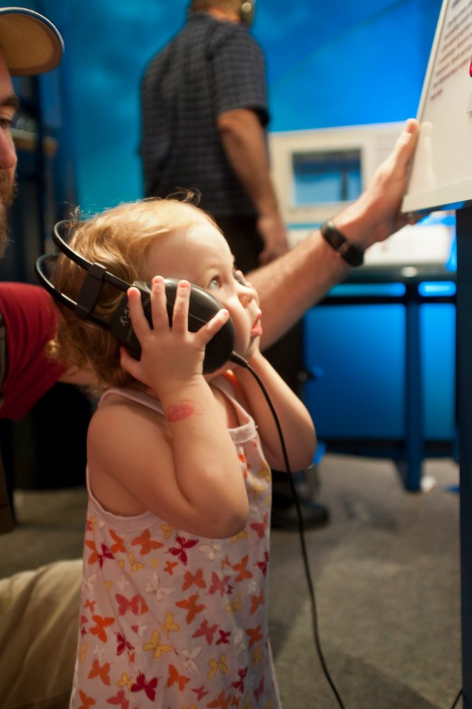 young child holds large headphones to her ears