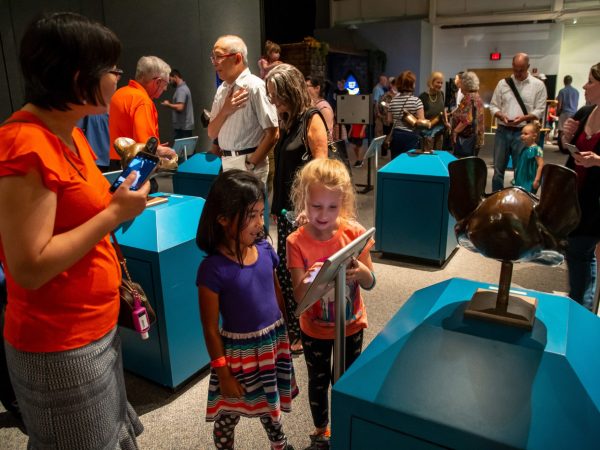 tow young children reading about an item on display, behind them are many people and displays in the bat exhibit