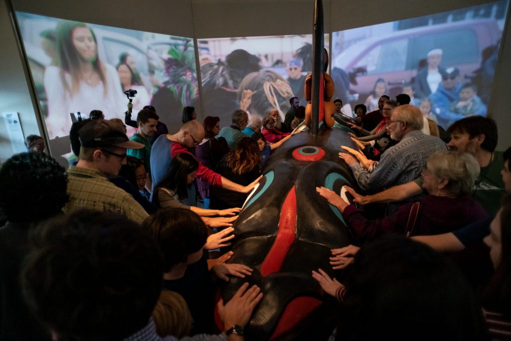 Visitors touch the totem during the opening of the “Whale People: Protectors of the Sea” exhibit. Unlike most objects in the museum, visitors are encouraged to touch the totem.