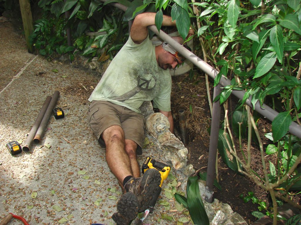 fabrication staff leaning over to repair a pipe in the rainforest exhibit