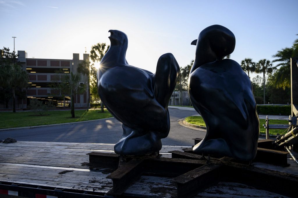 several large bird statues againt the sunrise with a parking garage in the background