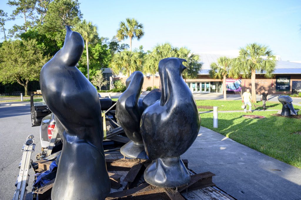 several large bird statues in a truck with people approaching another statue on the lawn