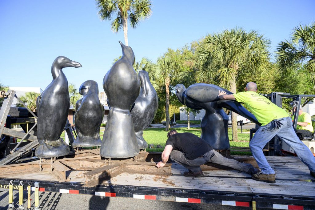 two men position one of several large bird statues in the back of a flatbed trailer