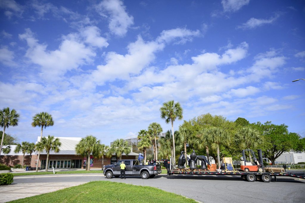 a flatbed trailer and pickup truck in front of the museum under a bright sky and clouds