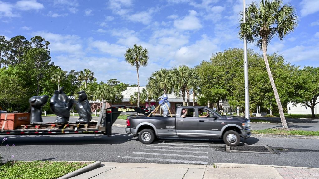 a flatbed trailer and truck driving past the museum while a passenger waves