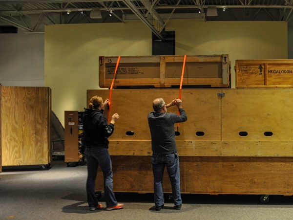 two people adjusting straps on a vary large wooden crate