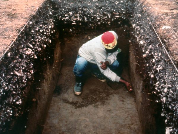 a person in a square excavation hole examines soil deposits