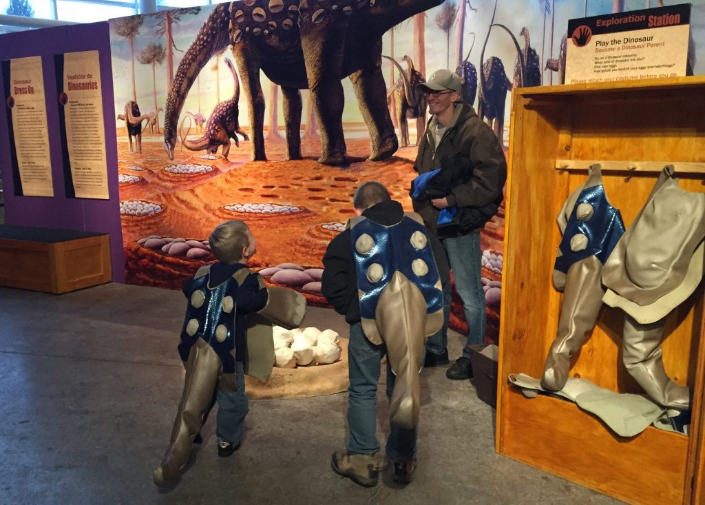 children in dinosaur costumes looking at mural