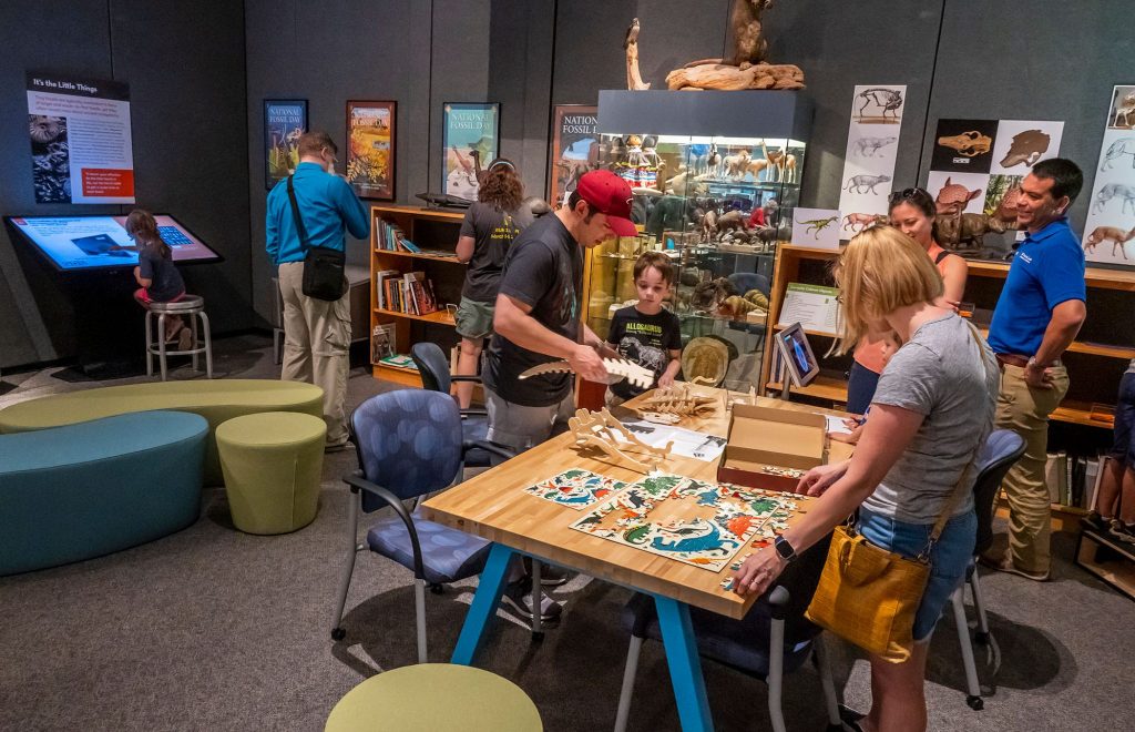 many people, adults and children standing around and playing with the fossil puzzles in the fantastic fossils exhibit