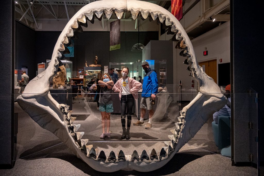 Two children posing for a photo behind the open fossil jaws of a megalodon