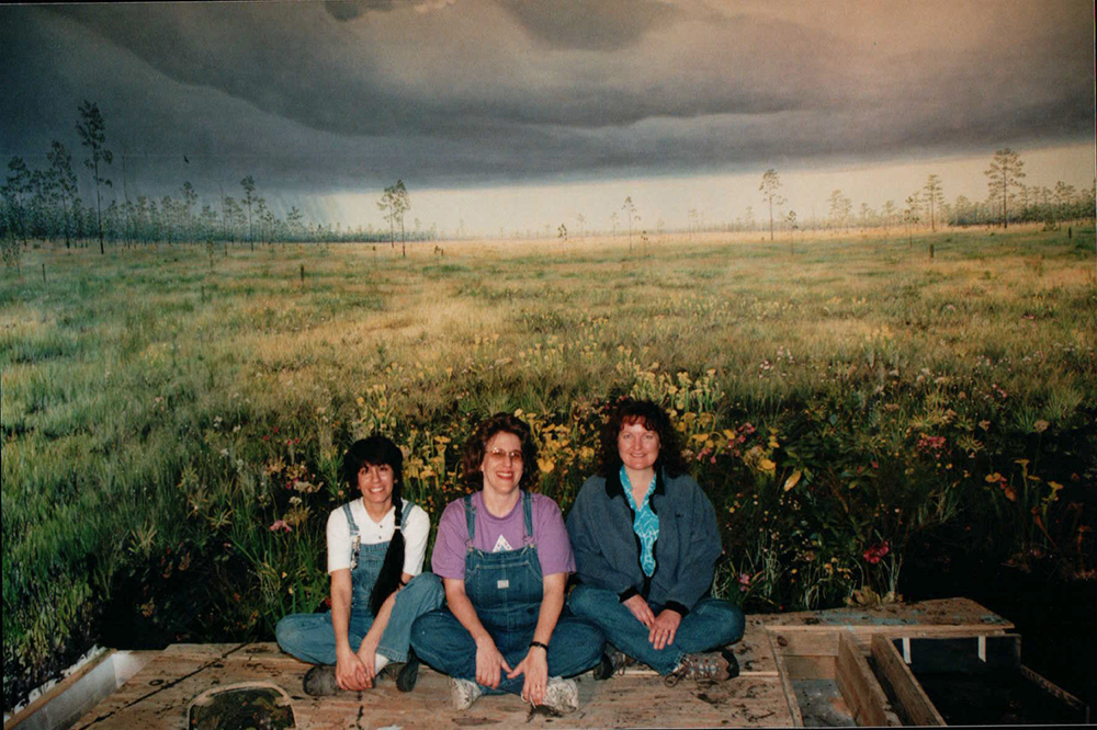 Three woman sit in front of mural