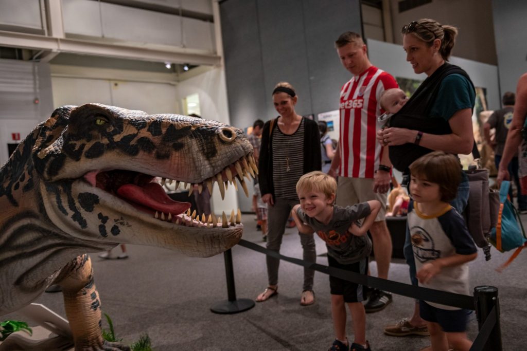 young children grin and lean close to a fabricated model of a large toothed predator on display in a museum exhibit