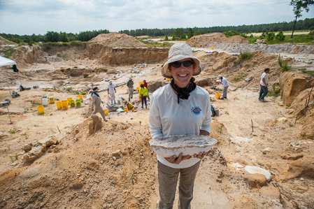 A volunteer holds a plaster jacket with the dig site in the background