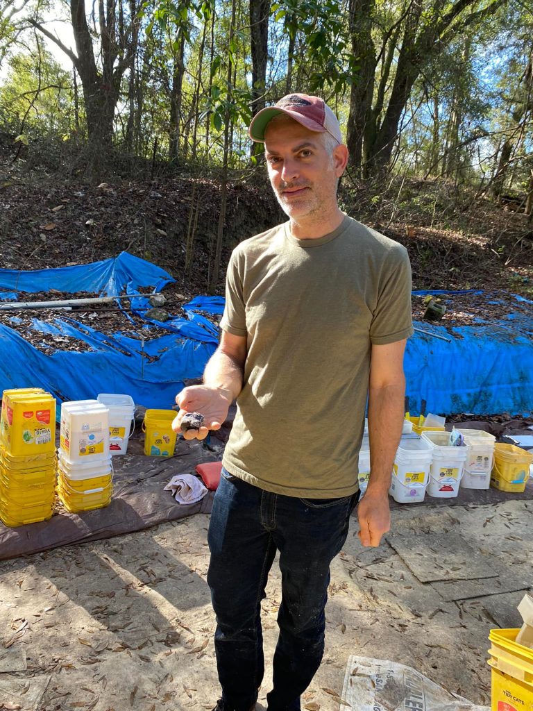 volunteer holdings fossil behind him you can see many buckets