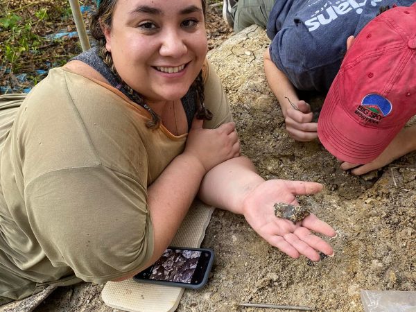 volunteers laying on ground holding a fossil and smiling at the camera