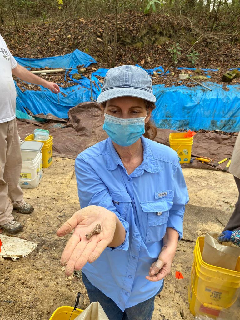 person wearing a mask holding out a hand with a fossil on it