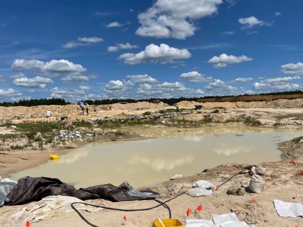 dig site partually covered in water after a heavy rain. Sky is rich bluw with white clouds