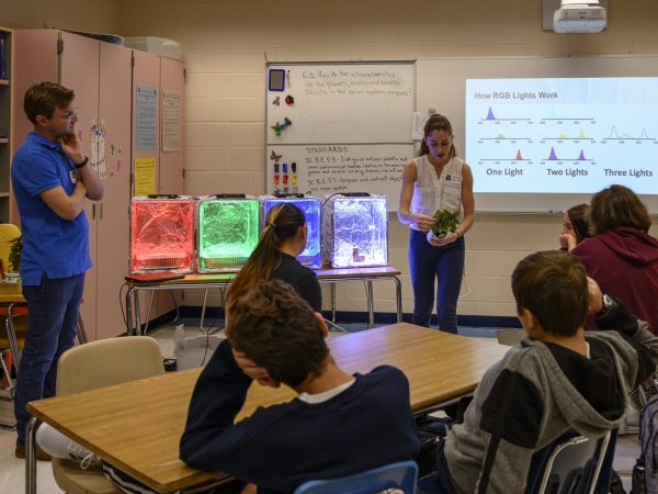 led light boxes in red green blue and white at front of room as scientist explains experiment