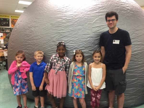 astrophysics scientist poses with several first graders in front of the Starlab