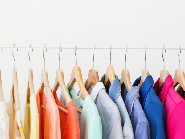 Clothing of many colors hanging from clothing rack.