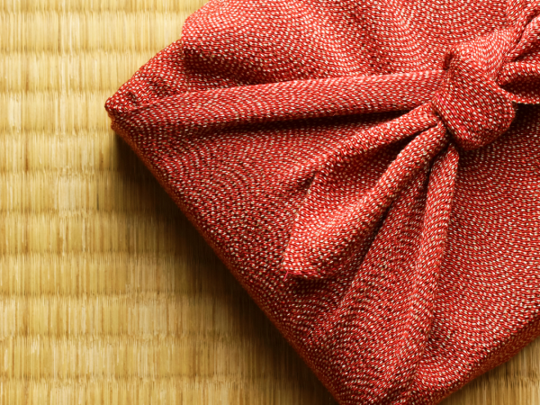 a gift wrapped in red glittery cloth on a tatami mat in the background