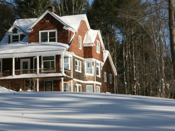 A multi-story brown house with snow covering the roof and the ground around the house.