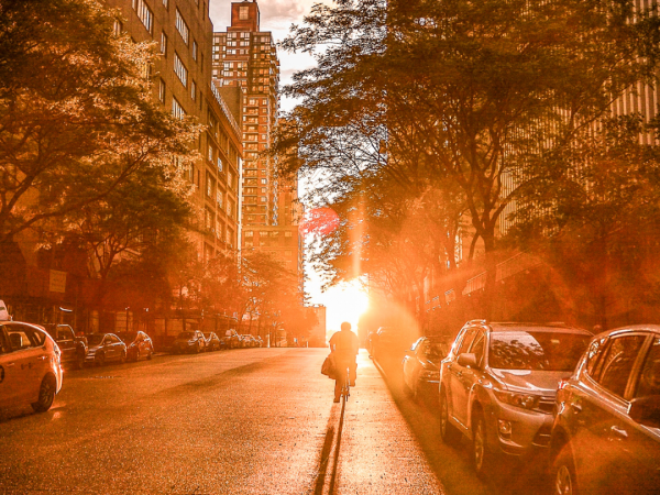 A street view with cars parked on the side of the street and tall office buildings in the distance. The street view converges with an orange colored lens flare in the center.