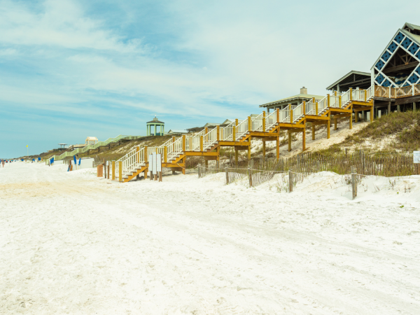 A wide shot of the steps leading down from a house up on a grassy slope to the sandy beach.