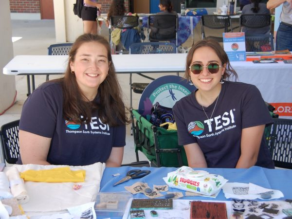 Two students in TESI t-shirts sit at a table at an outreach event.