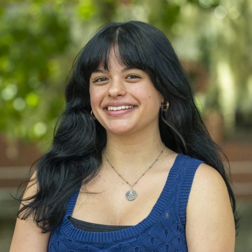 Kay smiling for her headshot in front of greenery at Dickinson Hall.